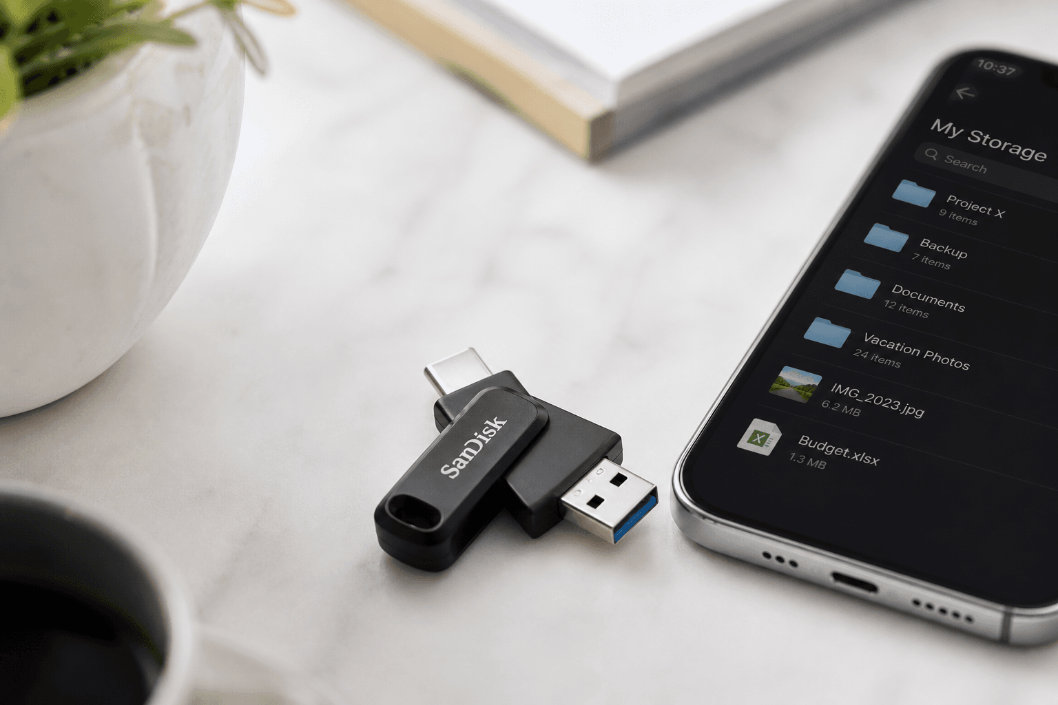 Pen USB com conectores USB-C e USB-A numa mesa de mármore, ao lado de um telemóvel que mostra uma lista de ficheiros