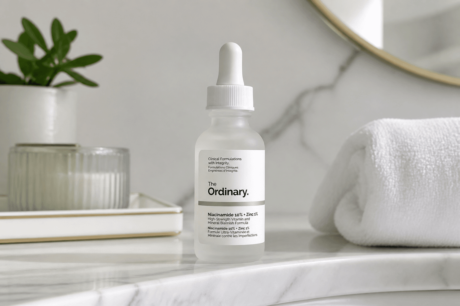 Frasco conta-gotas de sérum The Ordinary com niacinamida e zinco sobre mármore, junto a uma toalha branca e uma planta